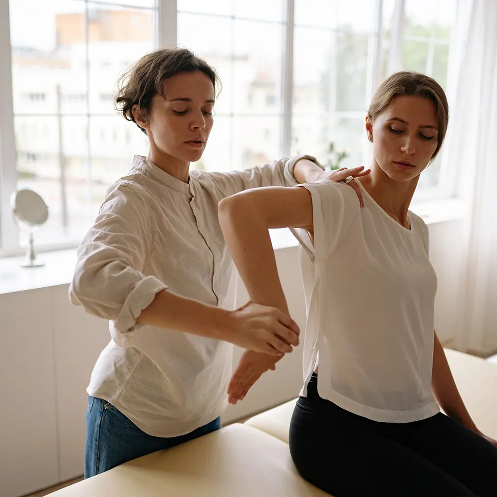 Therapist assessing a client's shoulder range of motion while the client sits on a treatment table during a functional capacity evaluation
