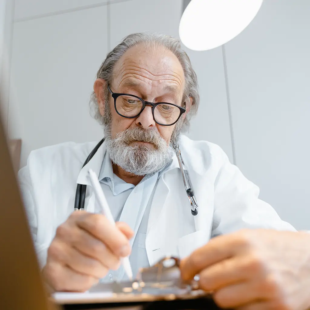 Physician in a white coat reviewing and writing notes on a clipboard during a medical file review